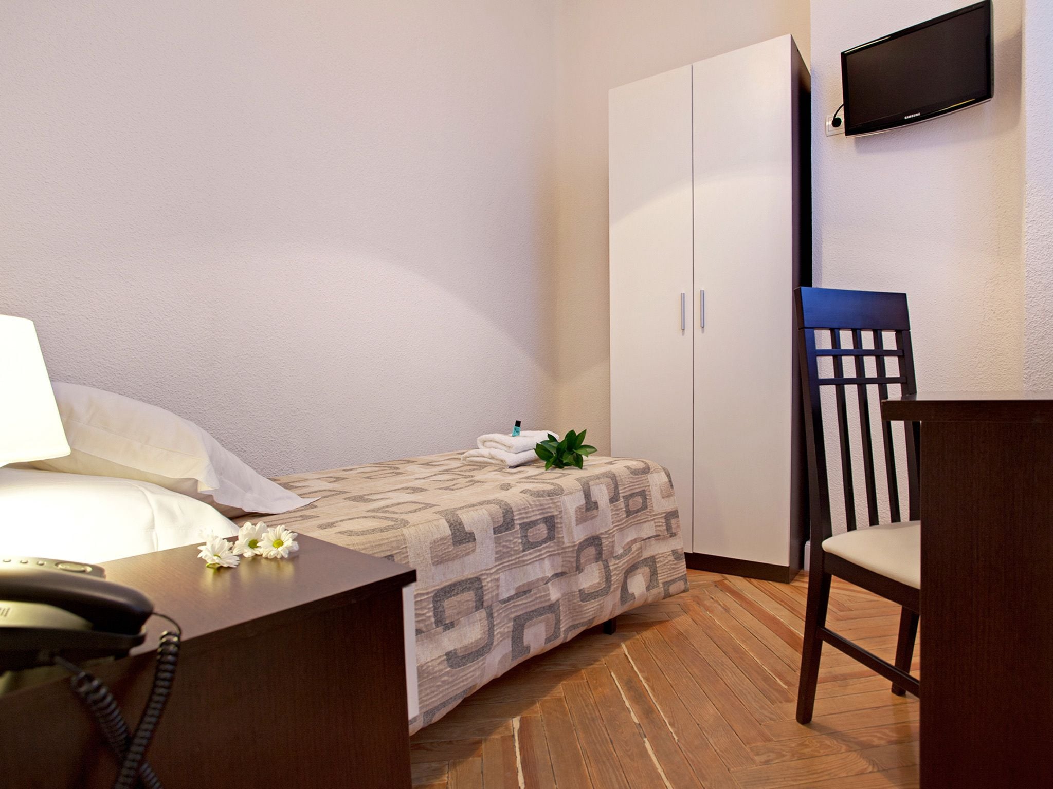 Une chambre d’hôtel comprenant un lit, un bureau avec un téléphone, une chaise, un téléviseur fixé au mur et une armoire.