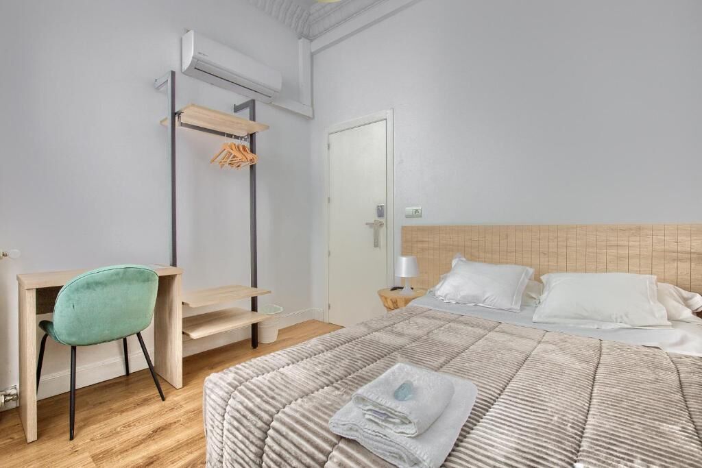 A bedroom with a bed, a desk, a chair, and a hanging clothes rack.