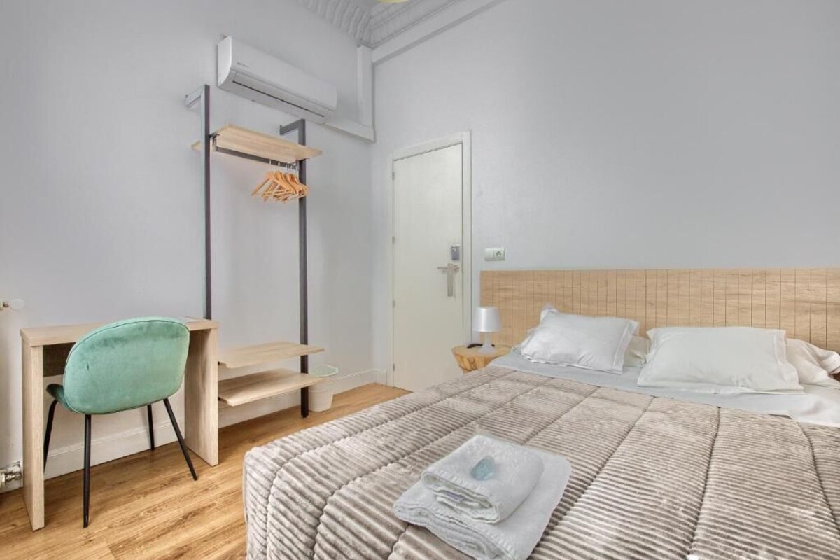 A bedroom with a bed, a desk, a chair, and a hanging clothes rack.