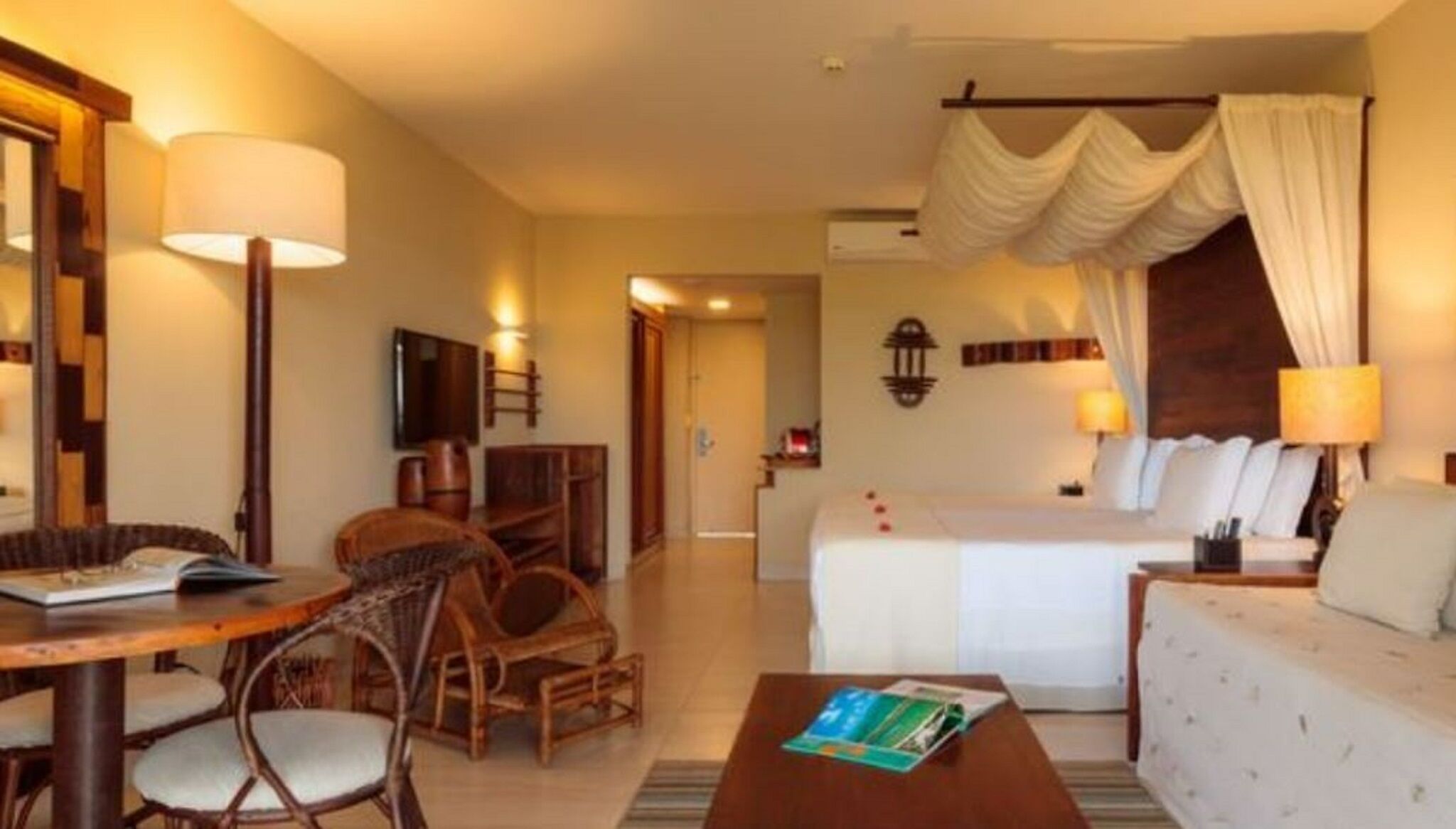 A hotel room with a bed, a sitting area with a table and chairs, a television, and a bathroom visible through an open door.