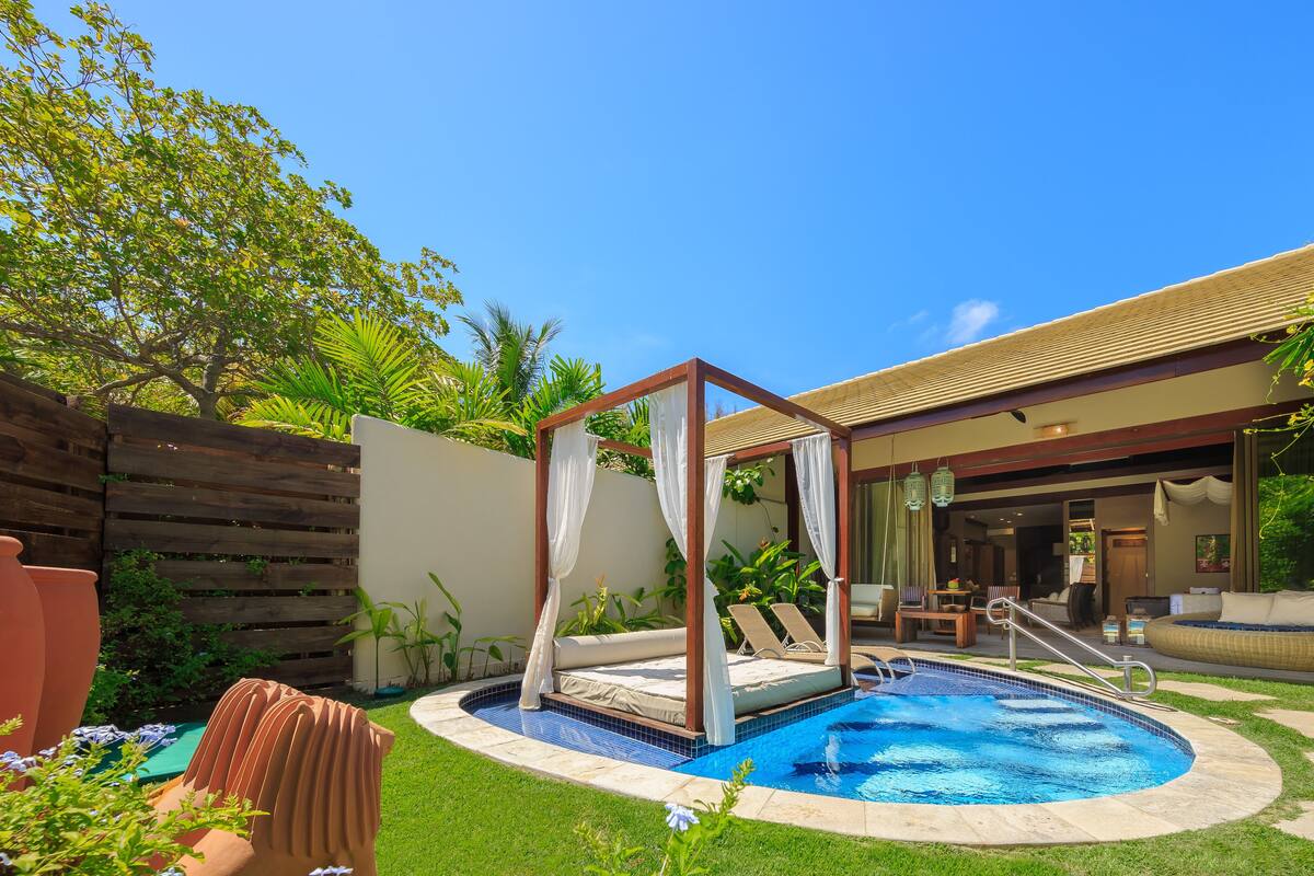 A backyard with a swimming pool, a wooden pergola, and a covered seating area.