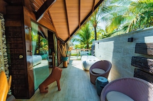 A covered outdoor area with wicker furniture, a glass door leading to a pool, and palm trees in the background.