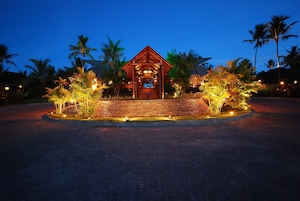 A wooden structure with a roof, surrounded by palm trees and illuminated by lights.