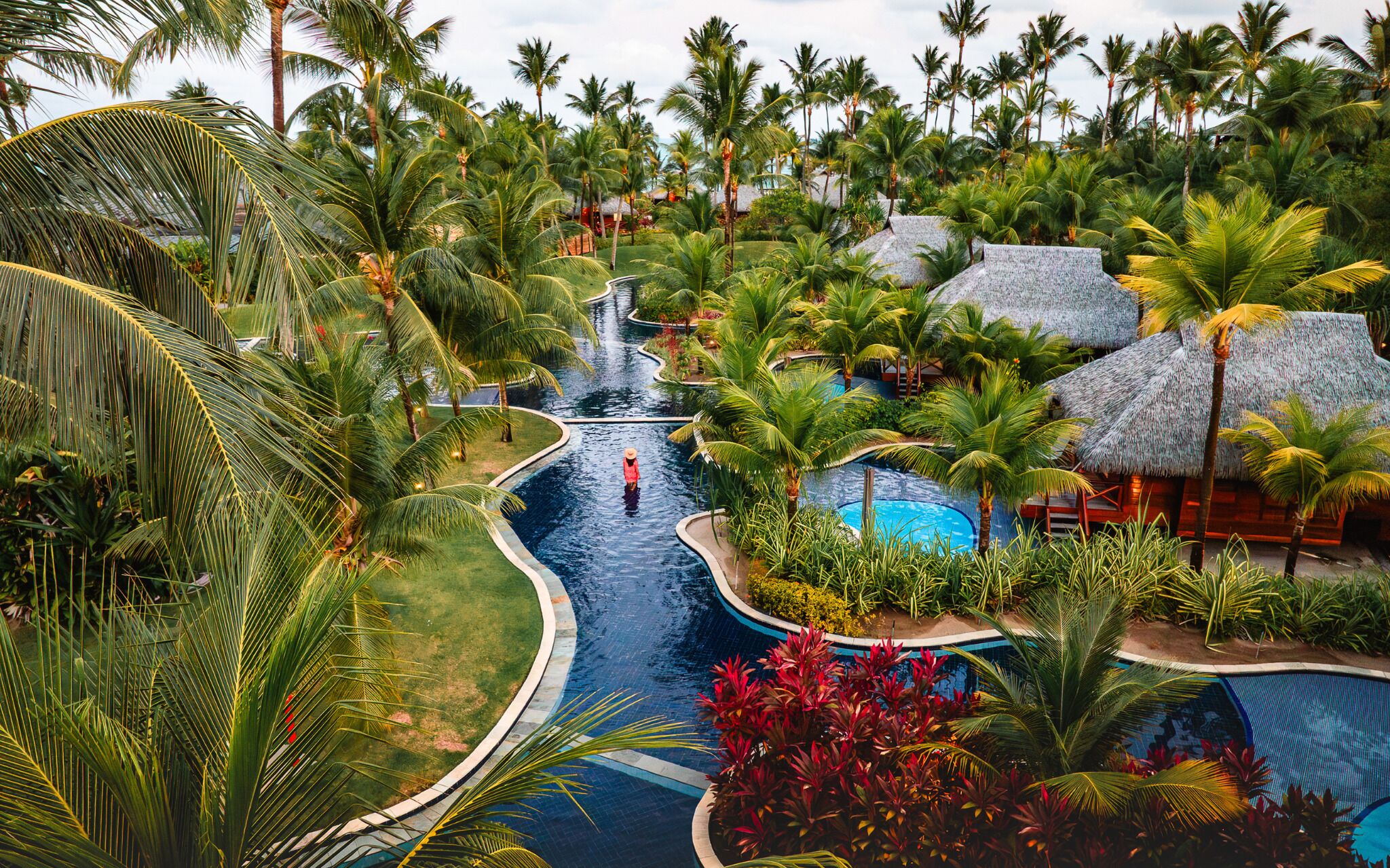 Un resort con piscina, palmeras y una estructura de techo de paja.