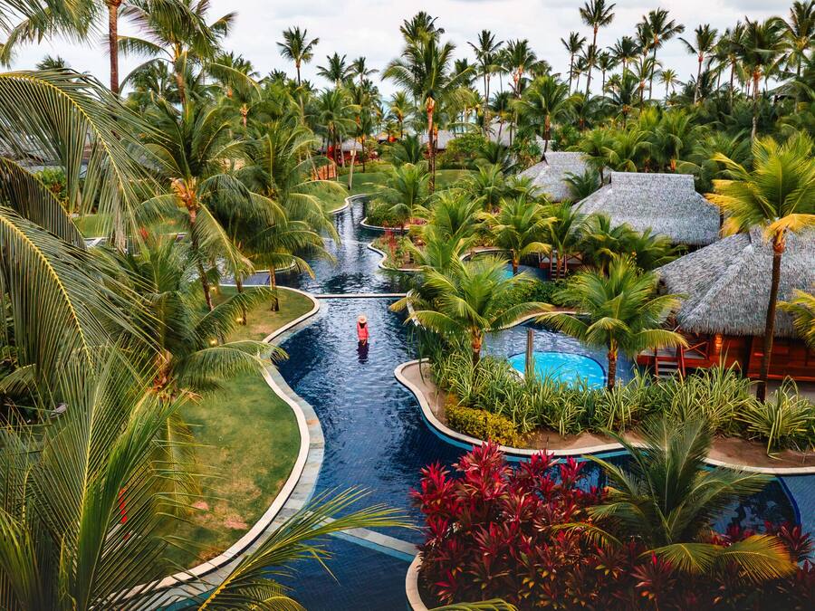 Un resort con piscina, palmeras y una estructura de techo de paja.