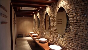 A row of sinks with mirrors, a stone wall, and a wooden bench. - NANNAI Muro Alto (Ipojuca)