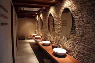A row of sinks with mirrors, a stone wall, and a wooden bench.