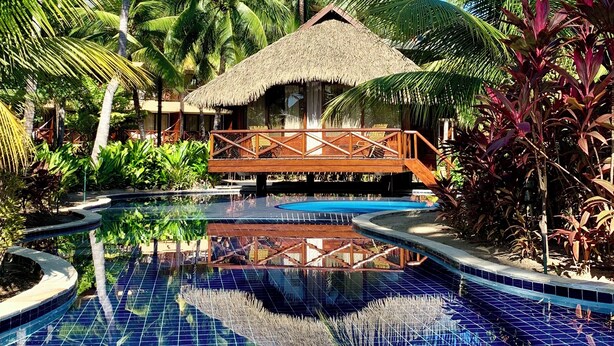 A resort pool with a thatched-roof structure and a wooden bridge. - NANNAI Muro Alto (Ipojuca)