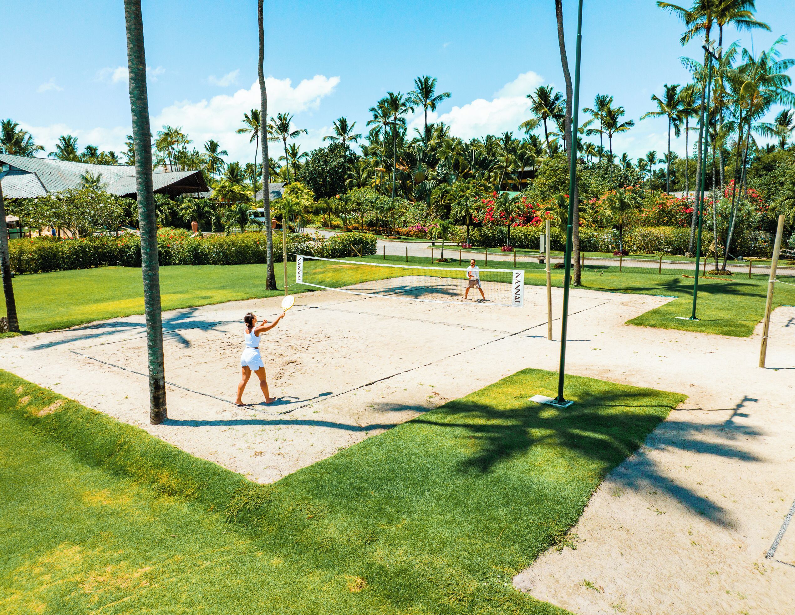 A tennis court with a net, surrounded by palm trees and greenery.