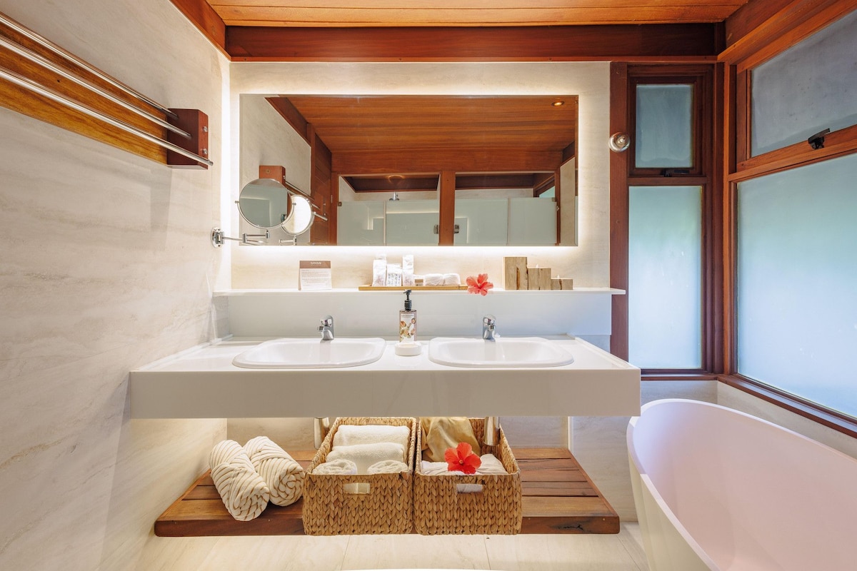 Un baño moderno con dos lavamanos, un espejo grande y una bañera independiente.