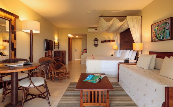 A hotel room with a bed, a sofa, a dining area with chairs, a table, and a small table with magazines.