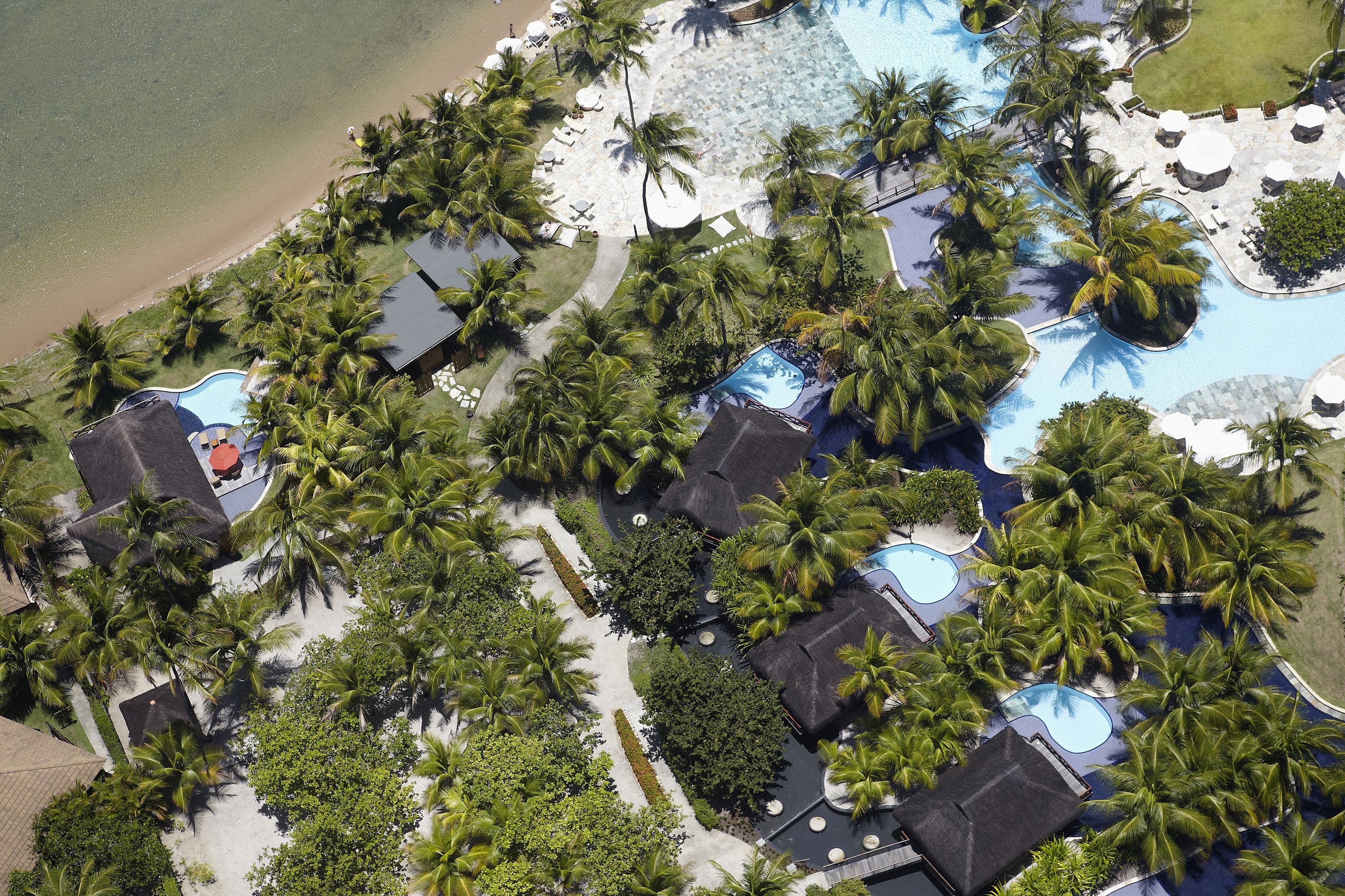 An aerial view of a resort with multiple swimming pools, palm trees, and beach access.