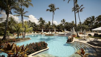 A resort pool area with palm trees, lounge chairs, and a clear blue sky.