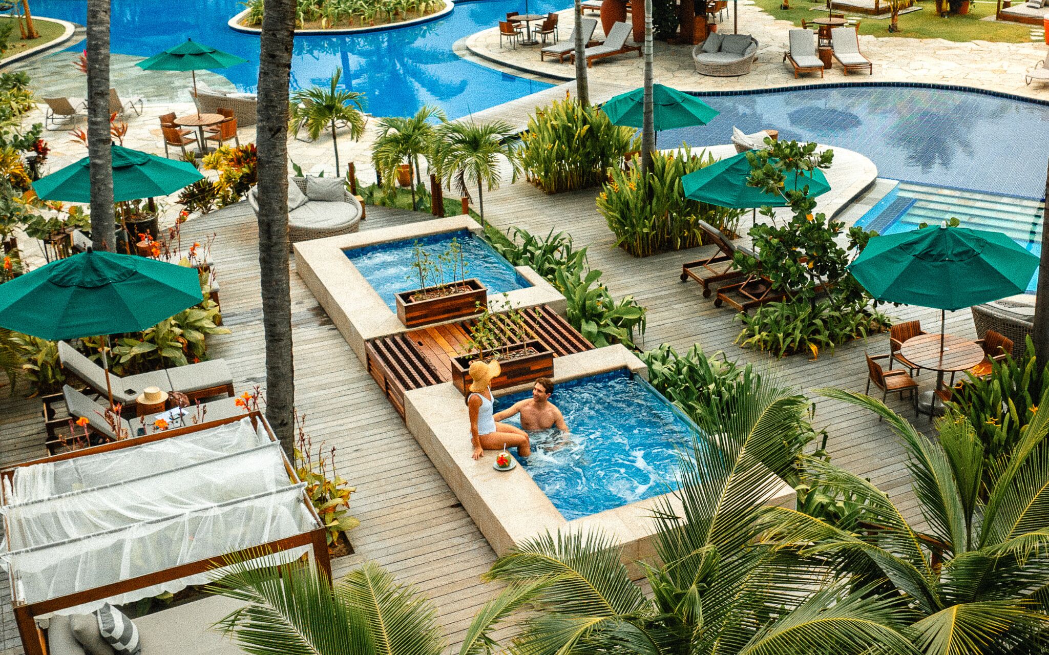 Área de piscina com várias piscinas, espreguiçadeiras e guarda-sóis.