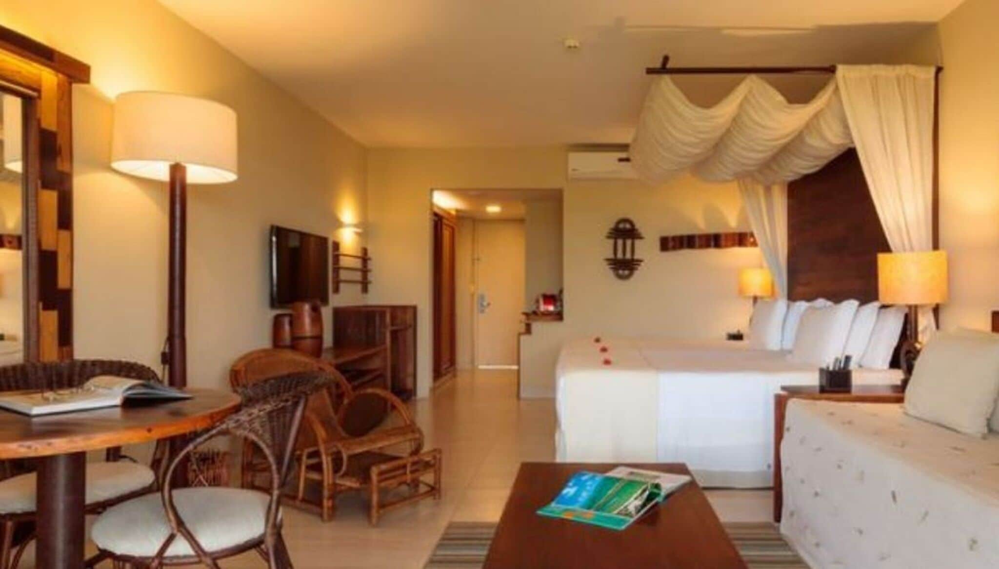 A hotel room with a bed, a sitting area with a table and chairs, a television, and a bathroom visible through an open door.