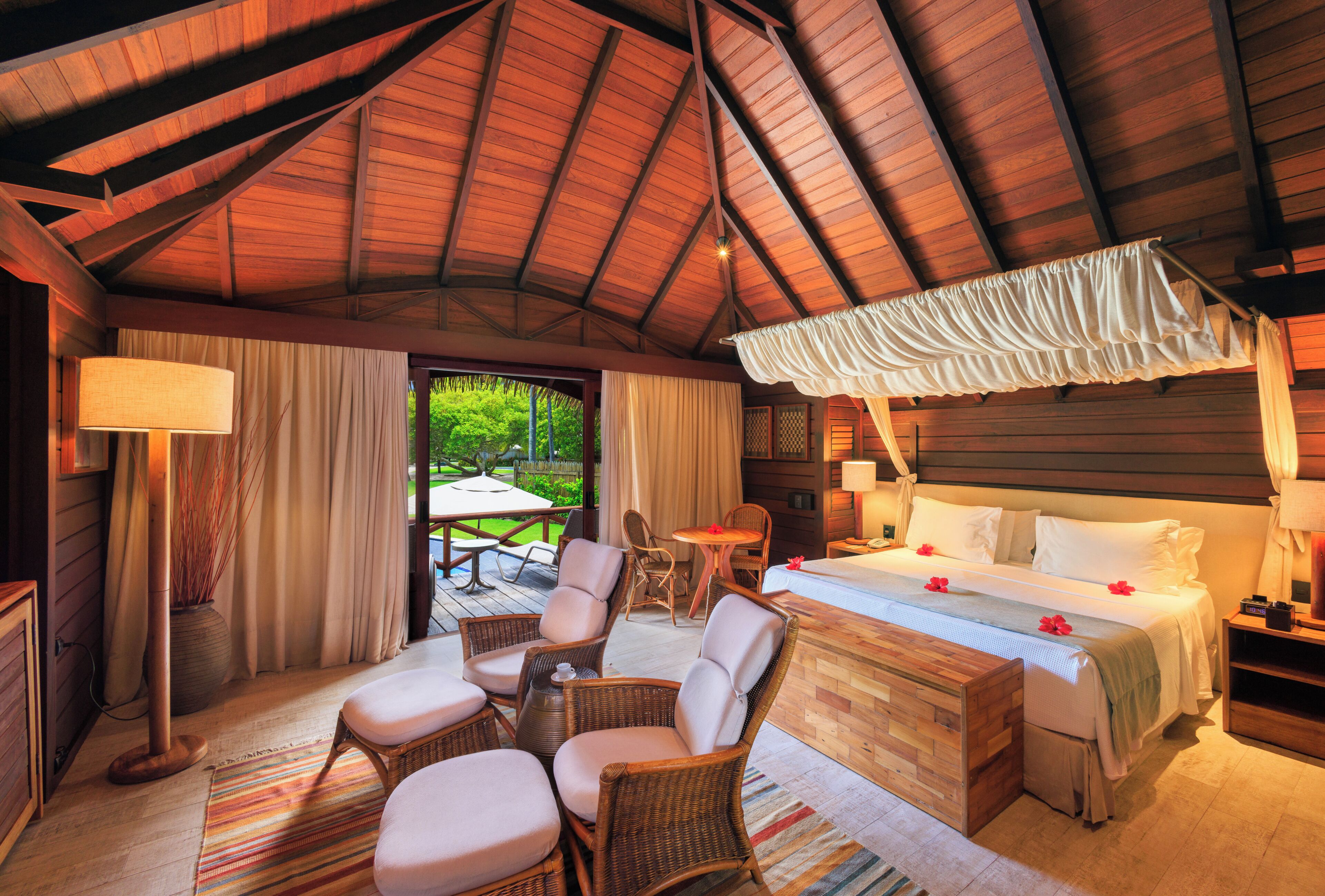 Un dormitorio amplio con una cama grande, un rincón de estar con sillas de mimbre y vistas al exterior.