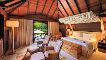 Un dormitorio amplio con una cama grande, un rincón de estar con sillas de mimbre y vistas al exterior.