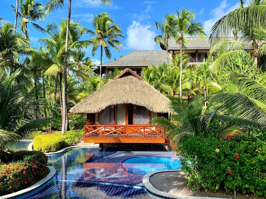 Un resort con piscina, palmeras y una estructura de techo de paja.
