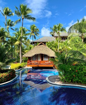 A resort with a swimming pool, palm trees, and a thatched-roof structure. - NANNAI Muro Alto (Ipojuca)