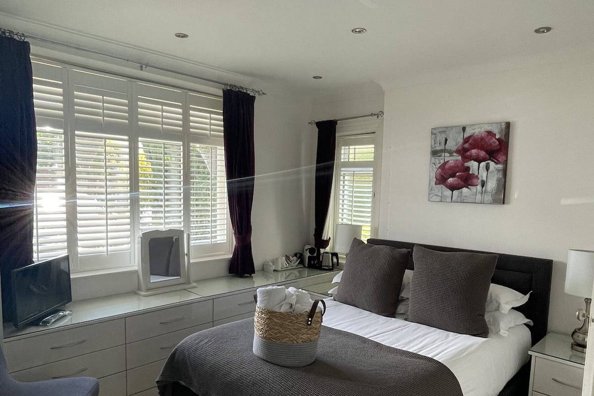 A bedroom with a bed, bedside table, lamp, TV, and a window with curtains.