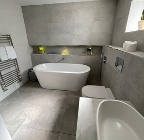 Un baño moderno con una bañera independiente, inodoro y zona de ducha.