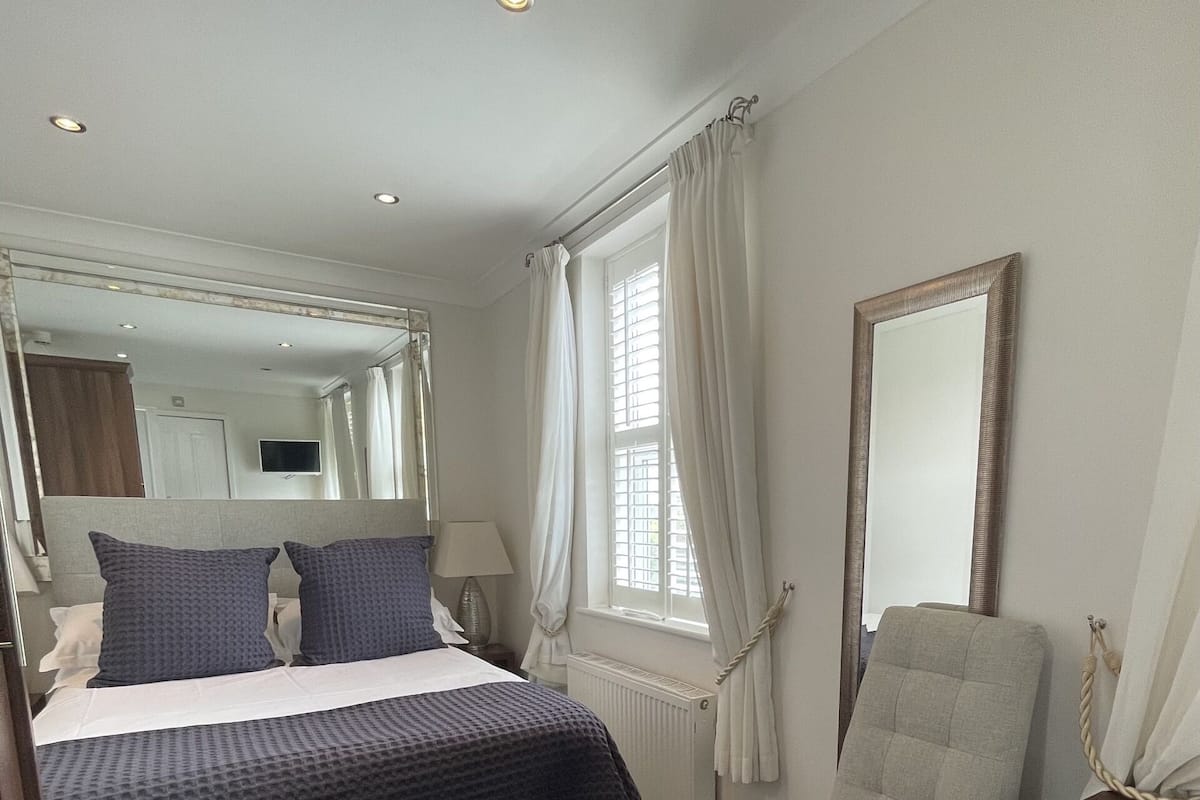 A bedroom with a bed, a chair, a dresser, a mirror, and a window with curtains.