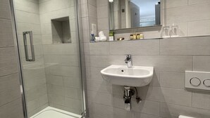 Un baño moderno con ducha acristalada, lavabo blanco y retrete.