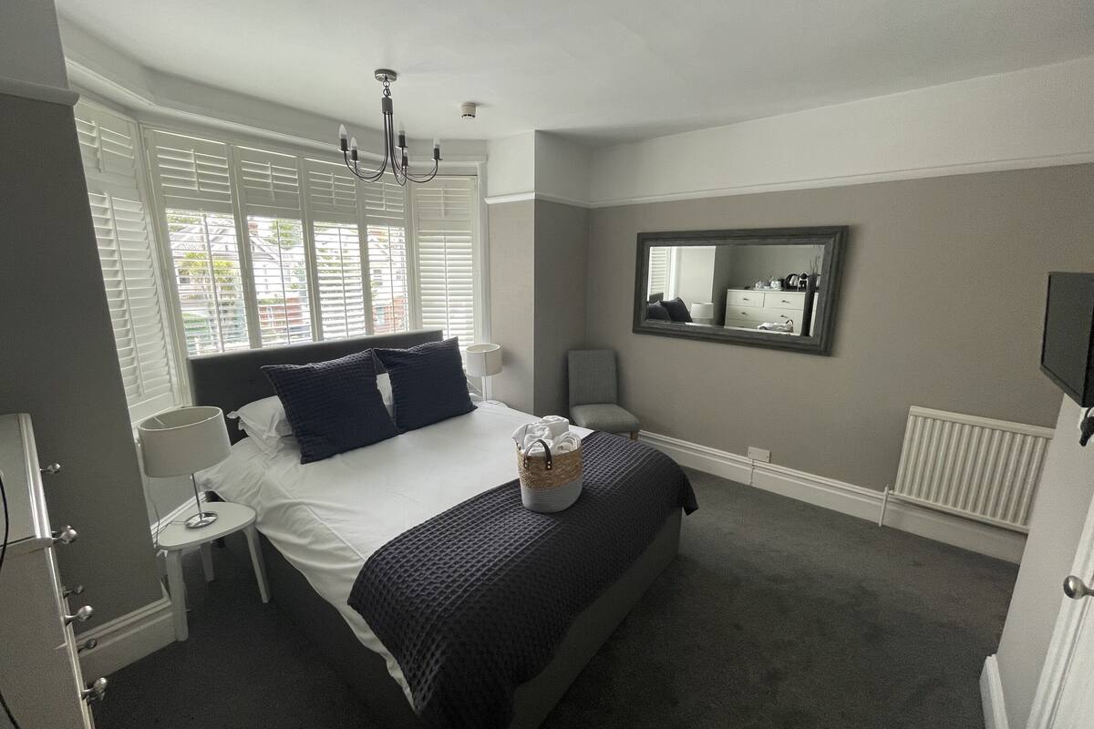 A bedroom with a bed, bedside tables, a mirror, and a window with blinds.