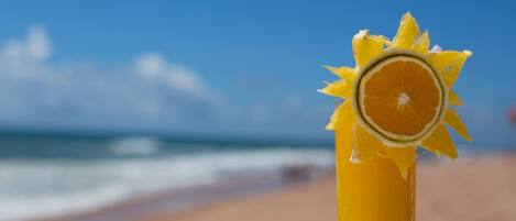 Un vaso alto de jugo de naranja con una rodaja de limón sobre una mesa, con vista al mar.