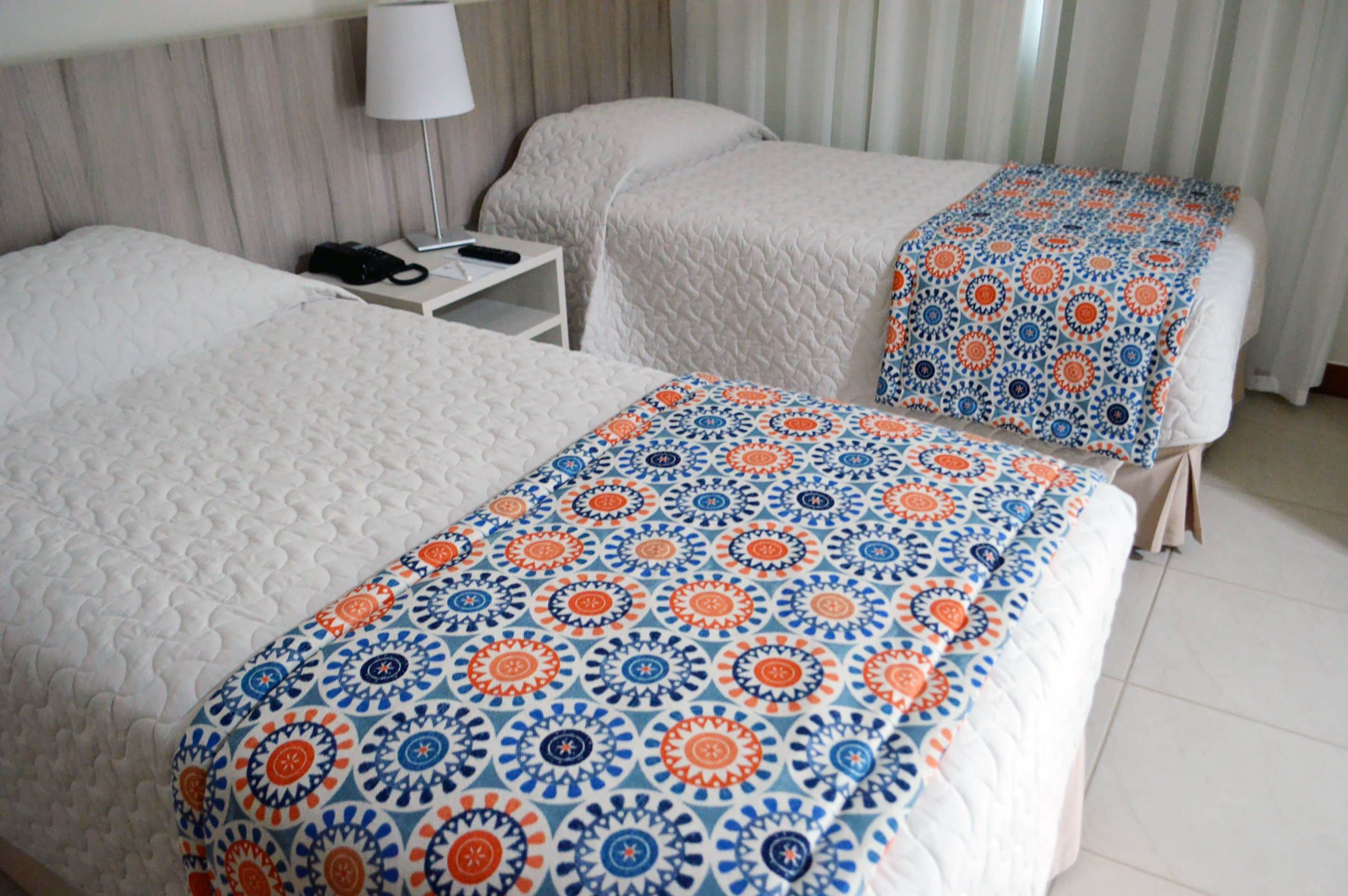 Una camera d'albergo con due letti, un comodino con una lampada e una coperta decorata.