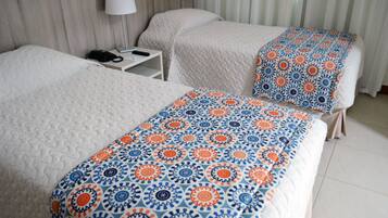 Una camera d'albergo con due letti, un comodino con una lampada e una coperta decorata.