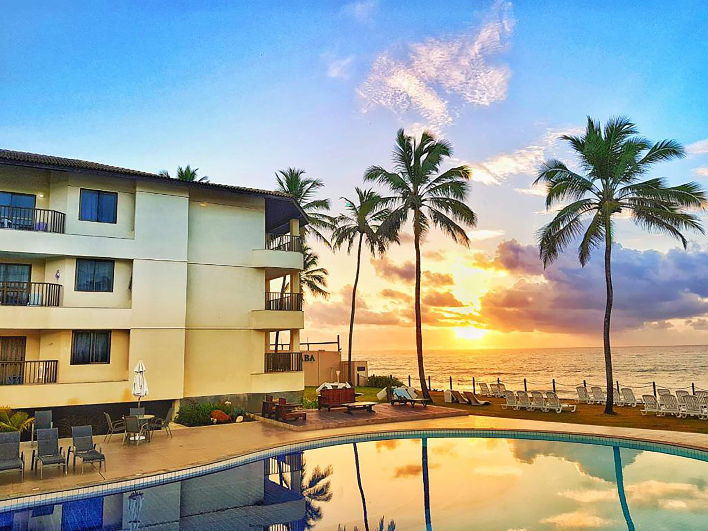 A hotel with a pool, palm trees, and a sunset view.
