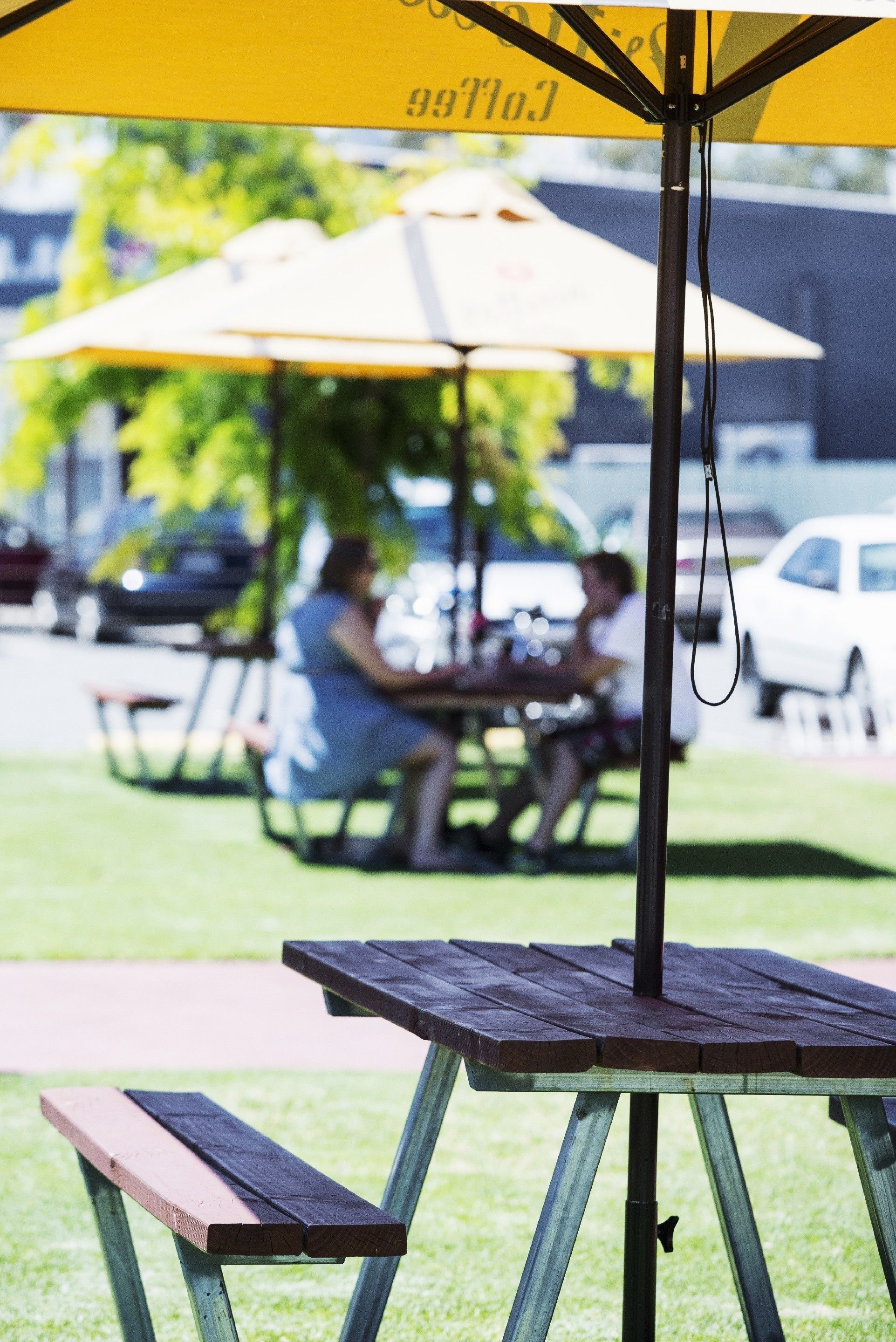 Een picknicktafel met een gele parasol, een metalen standaard en een houten bank.