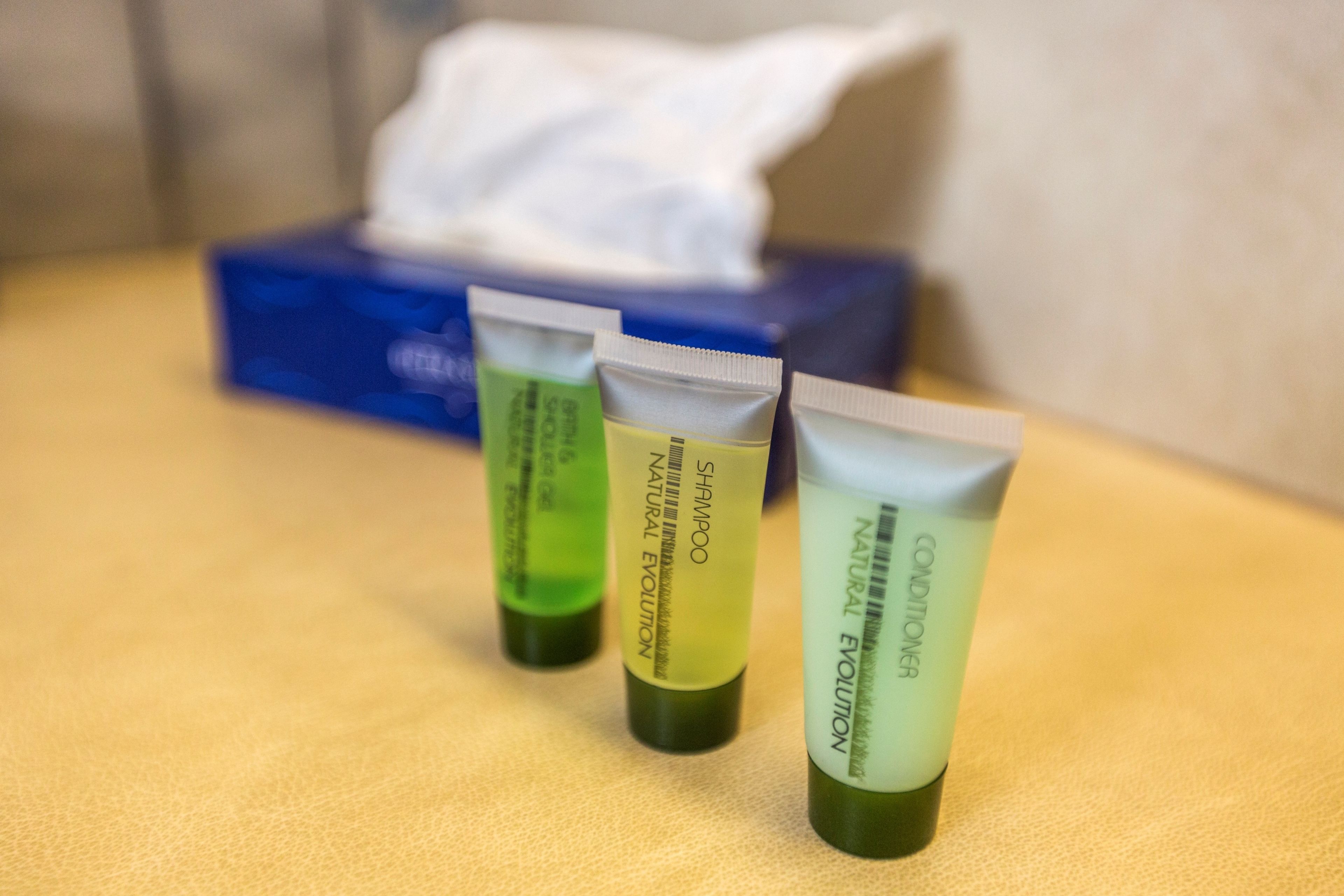Three tubes of shampoo and conditioner on a table with a tissue box in the background.