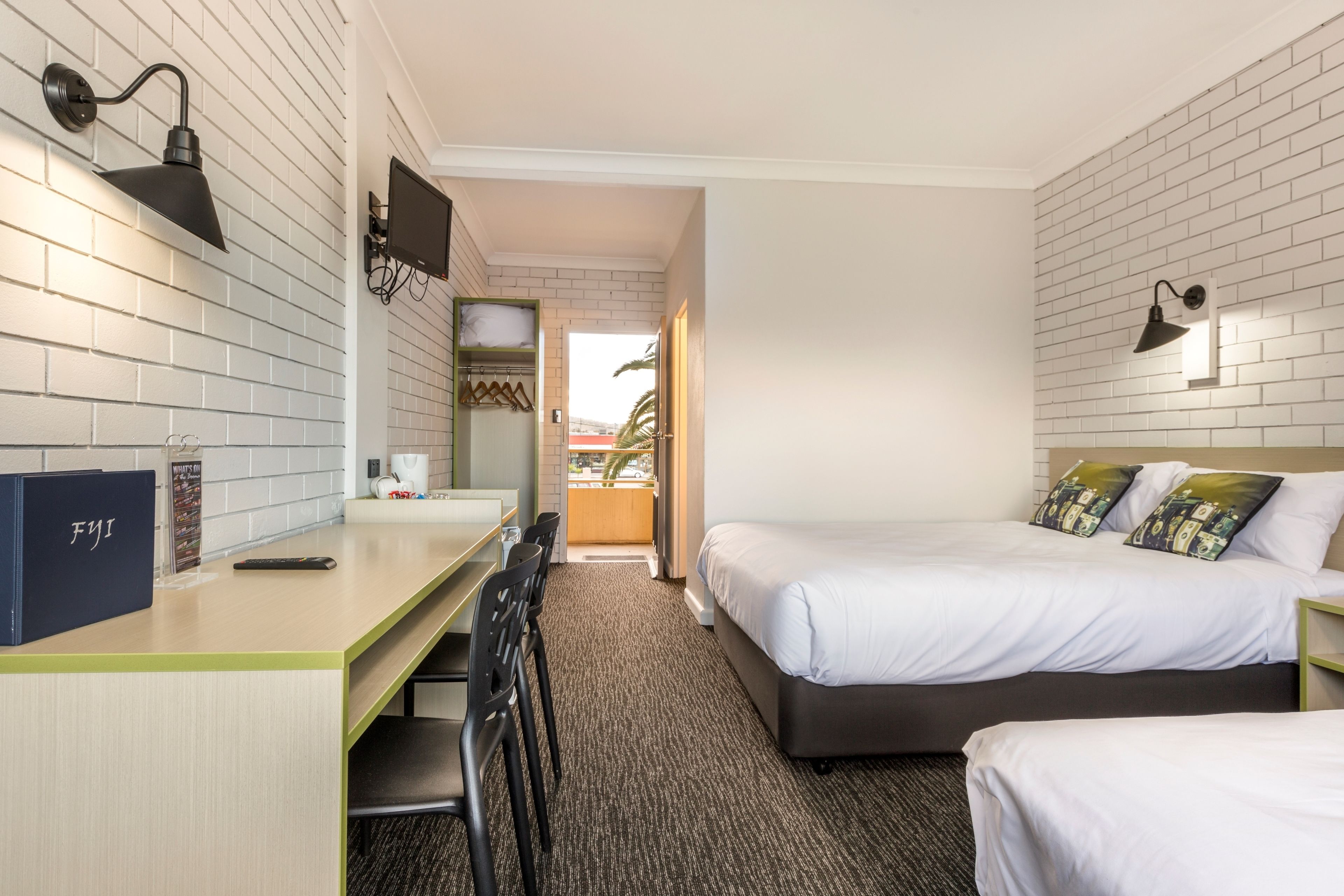 A hotel room with a desk, two beds, a TV, and a view of the outdoors.