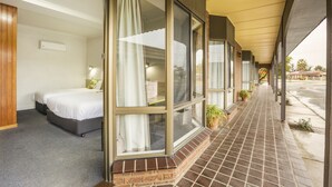 A hotel room with a bed, a window with curtains, a small table, and a potted plant. - Boomerang Hotel (Lavington)