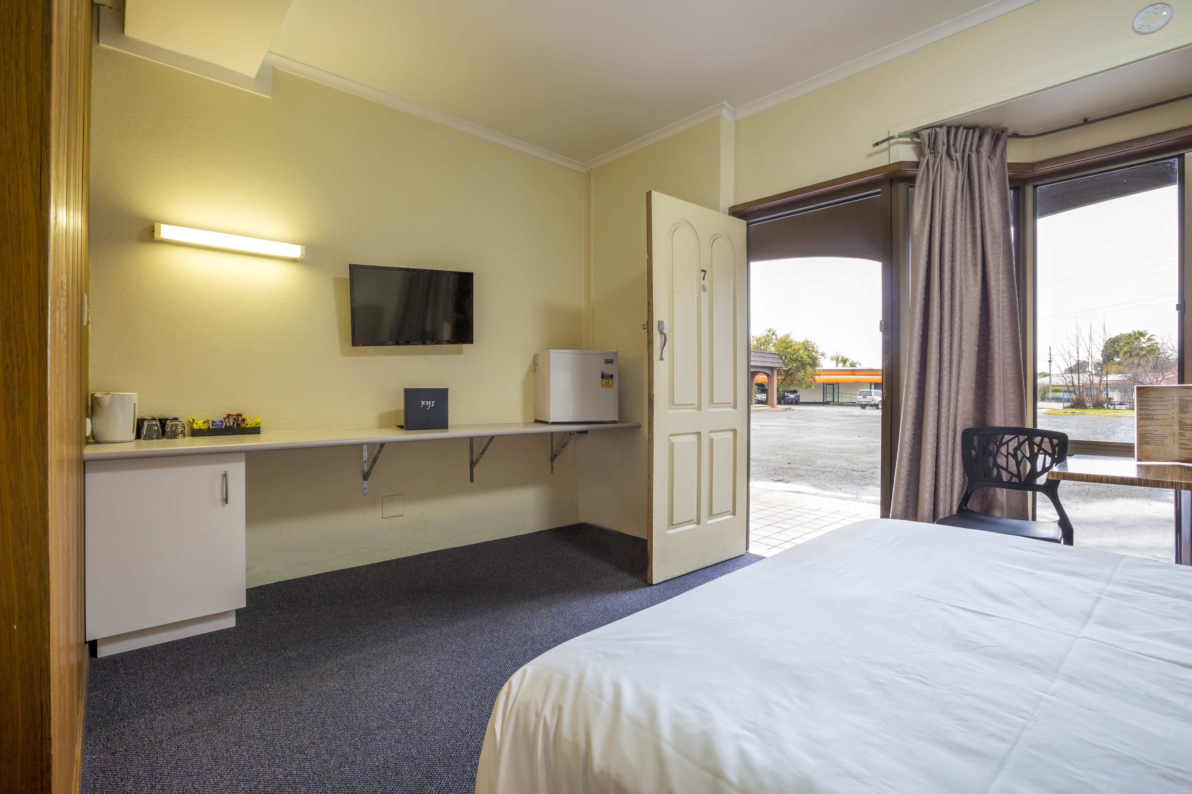 Una habitación de hotel con una cama, un escritorio con computadora, televisión y ventana con cortinas.