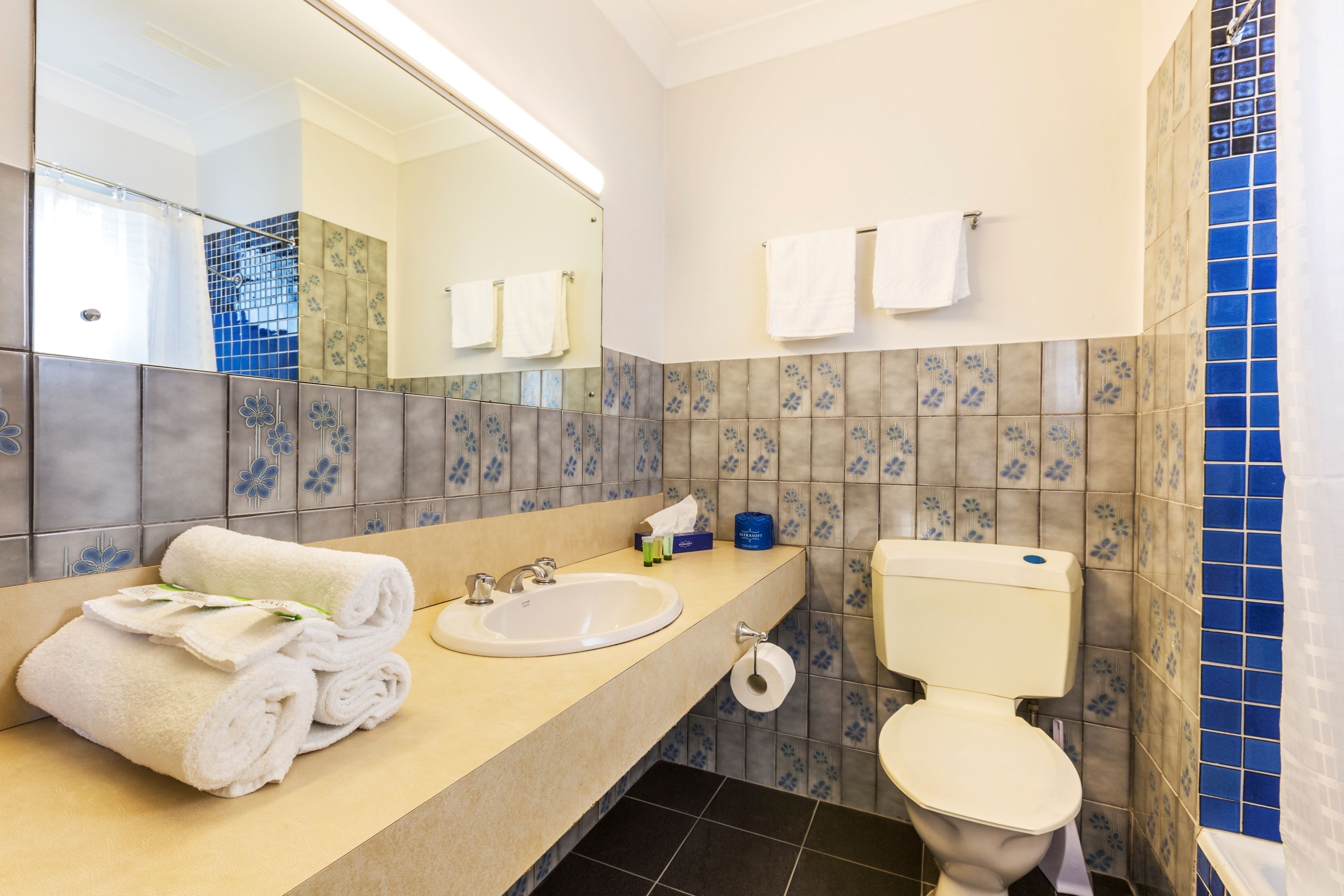 A bathroom with a sink, toilet, and a mirror. There are towels stacked on the sink counter.
