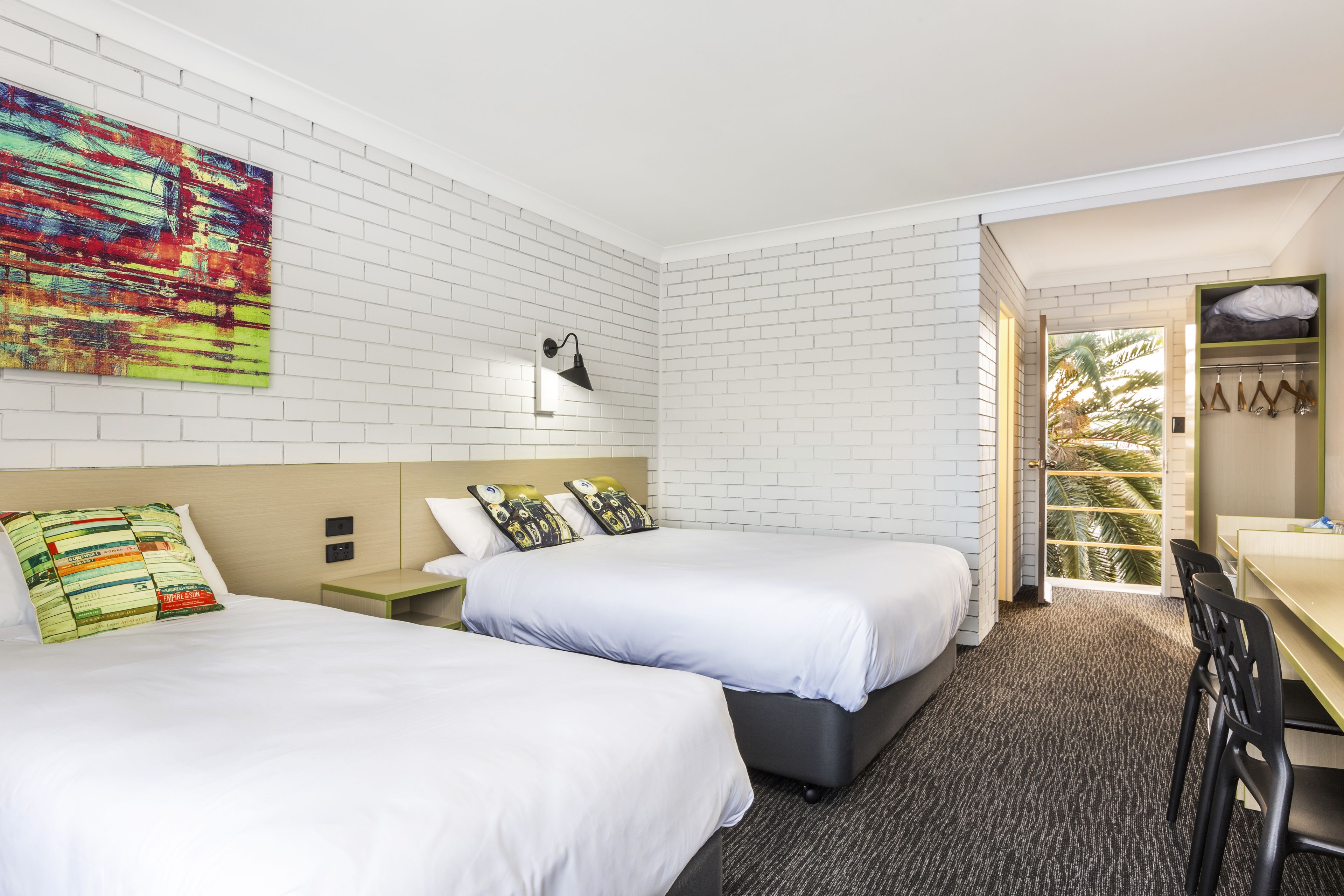 Habitación de hotel con dos camas, un escritorio y vistas a palmeras.