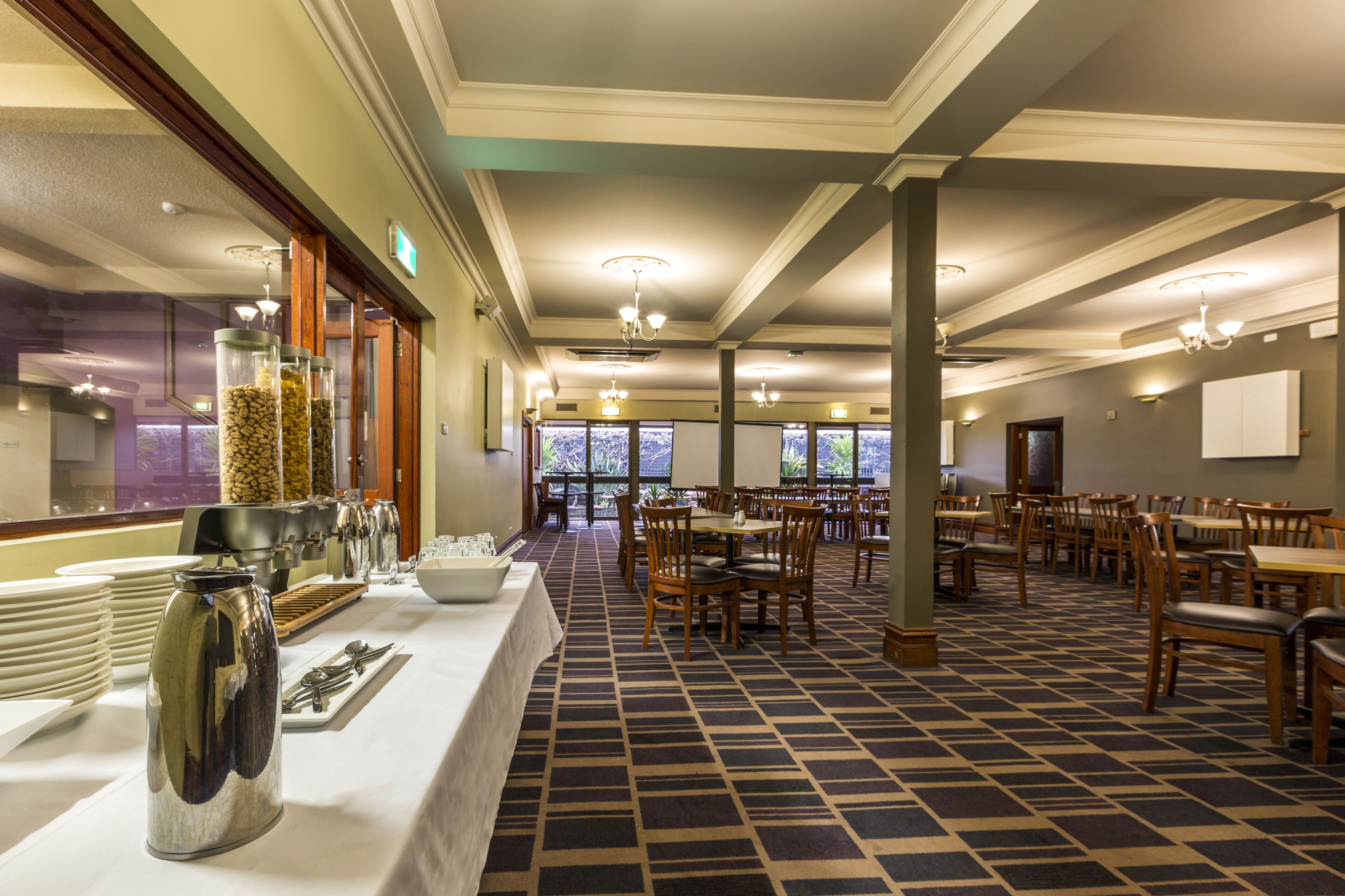 A hotel dining area with a buffet setup, multiple tables, and chairs.