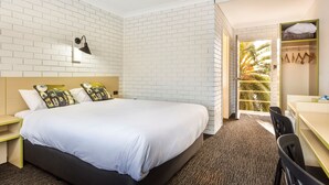 A hotel room with a white brick wall, a bed with white bedding, a desk with a chair, and a wardrobe. - Boomerang Hotel (Lavington)