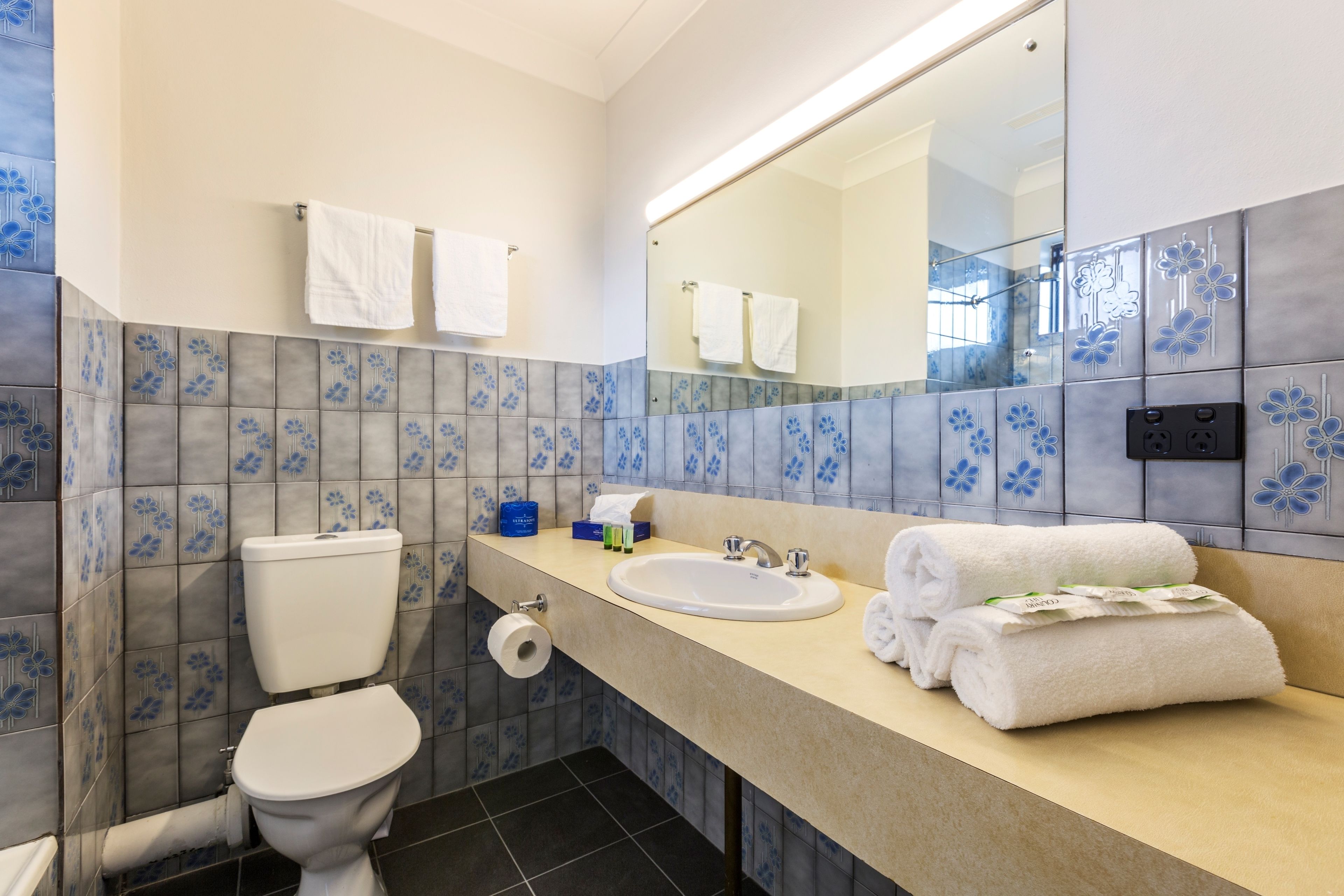 A bathroom with a toilet, sink, and mirror. There are towels and toiletries on the sink counter.