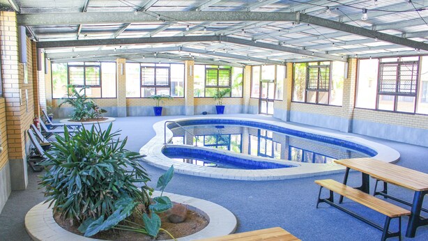 An indoor swimming pool with benches and potted plants. - Boomerang Hotel (Lavington)