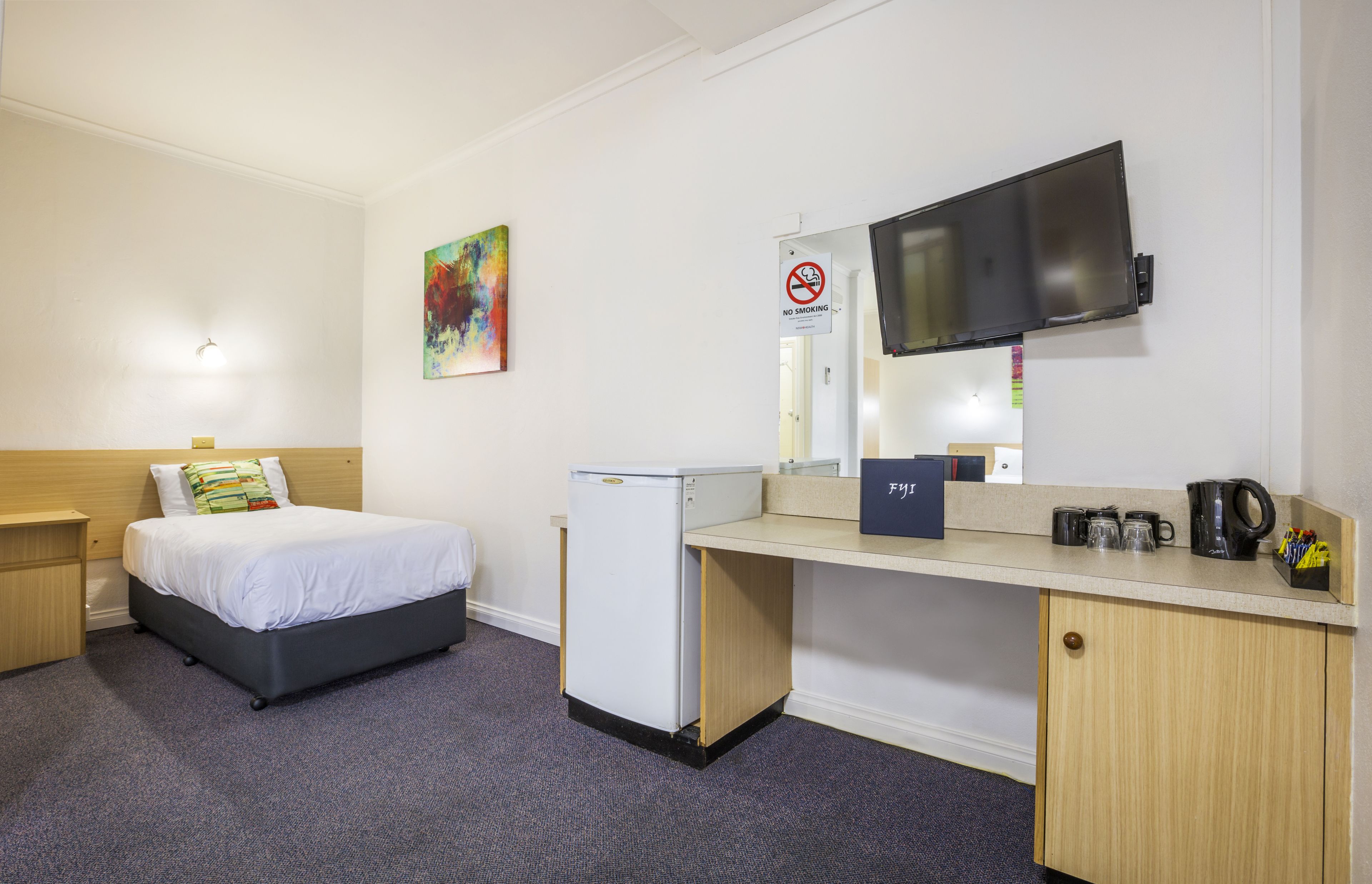 Habitación de hotel con cama, escritorio, refrigerador, televisor y un cartel de 'No Fumar'.
