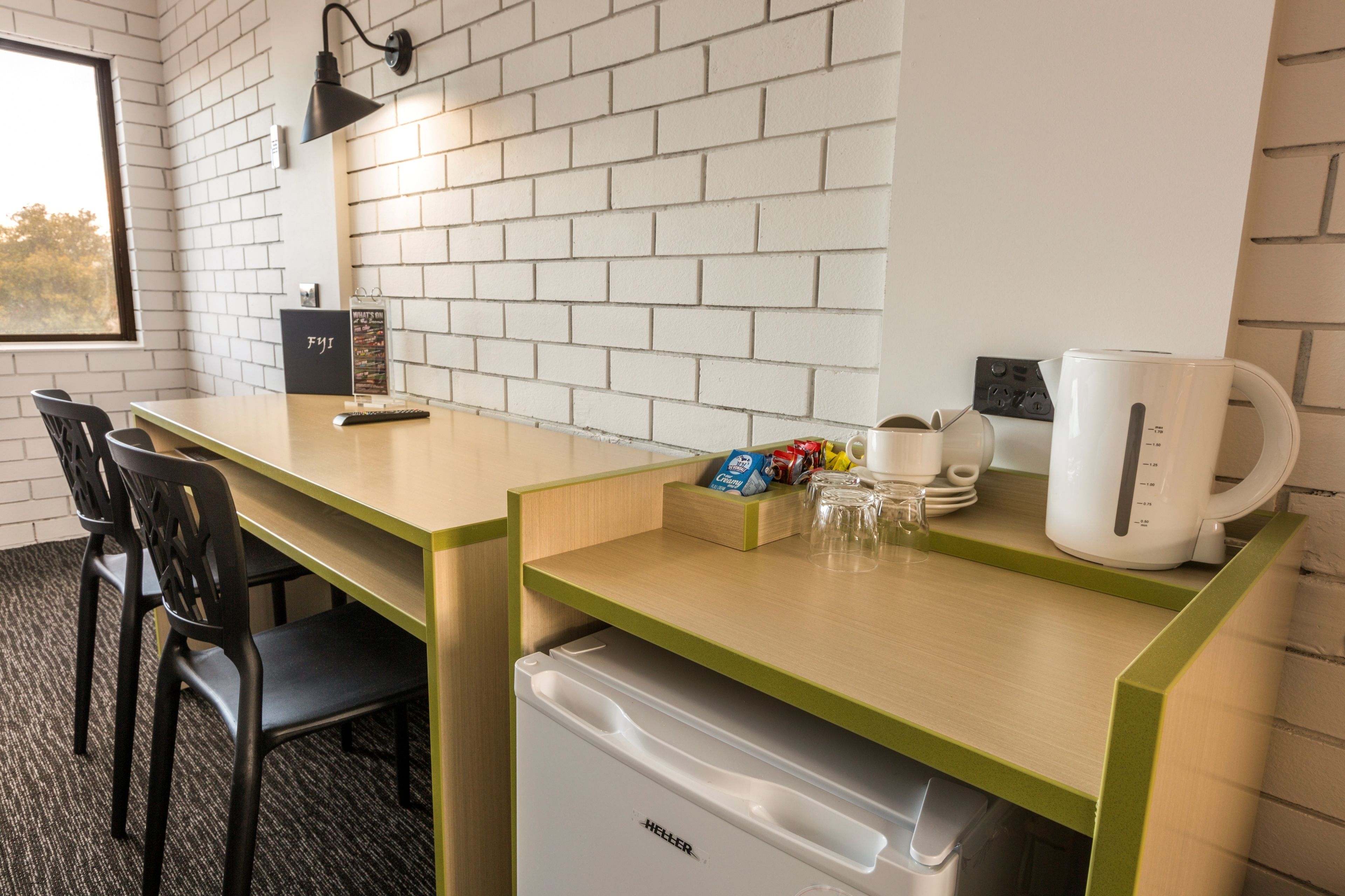 Habitación de hotel compacta con kitchenette, un pequeño refrigerador, cafetera y ventana con vistas.