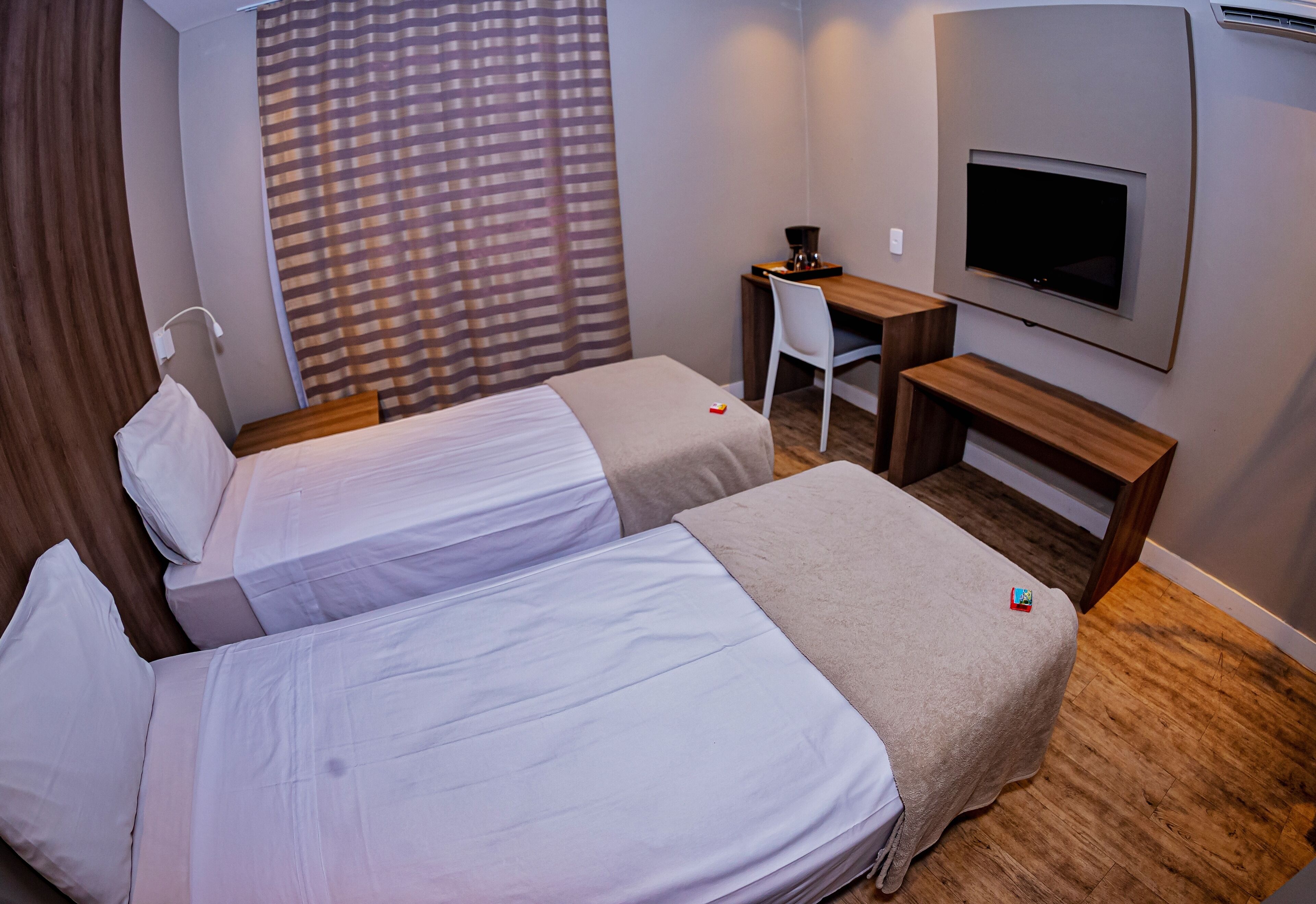 Une chambre d’hôtel avec deux lits, un bureau, une chaise, une télévision et une fenêtre avec des rideaux.