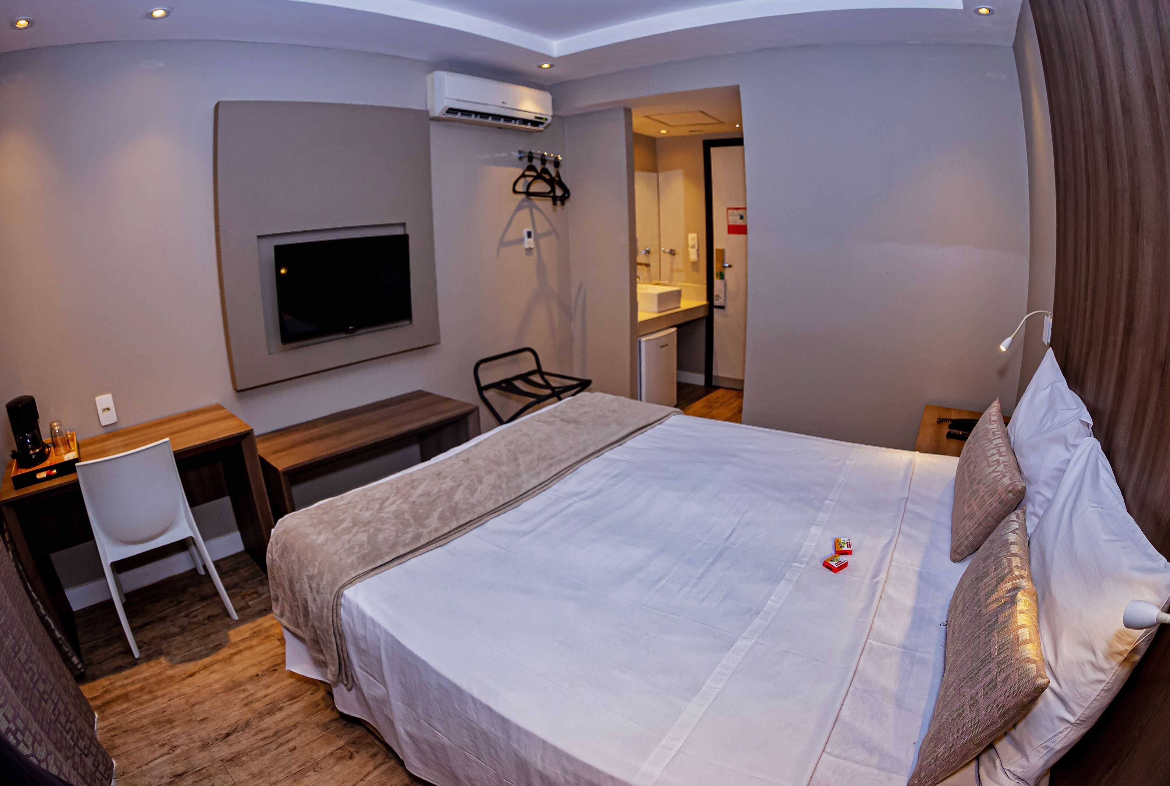 A hotel room with a bed, a desk, a chair, a TV, and a kitchenette.
