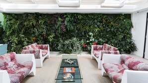 A modern lounge area with white sofas and a glass coffee table, a green wall with plants, and a ceiling with skylights. - The Hotel (Salvador)