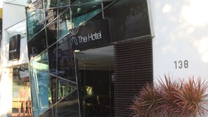 A modern hotel entrance with glass facade, a sign reading "The Hotel", and the number 138 on the wall. - The Hotel (Salvador)