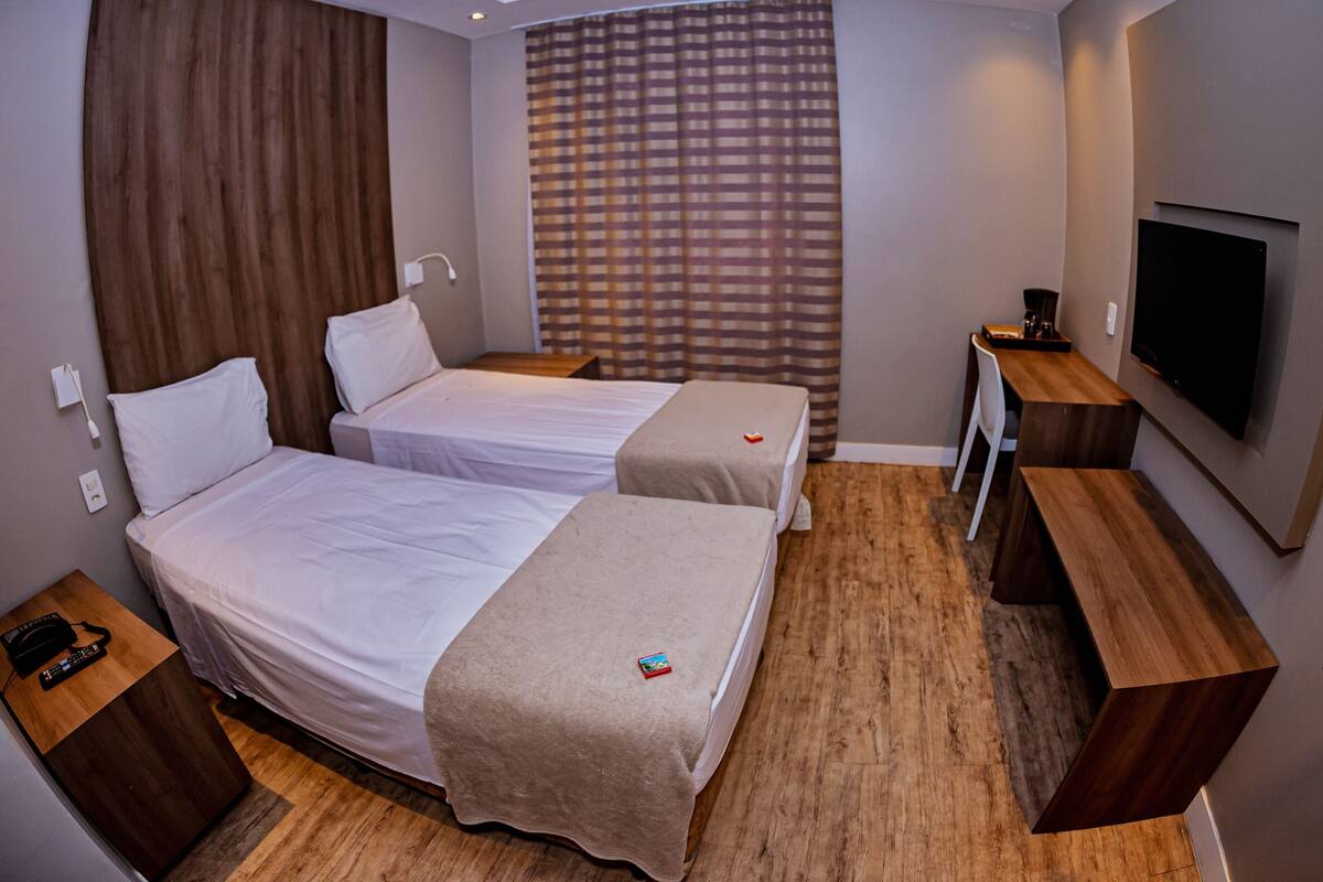 Ein Hotelzimmer mit zwei Betten, einem Fernseher, einem Schreibtisch und Holzboden.